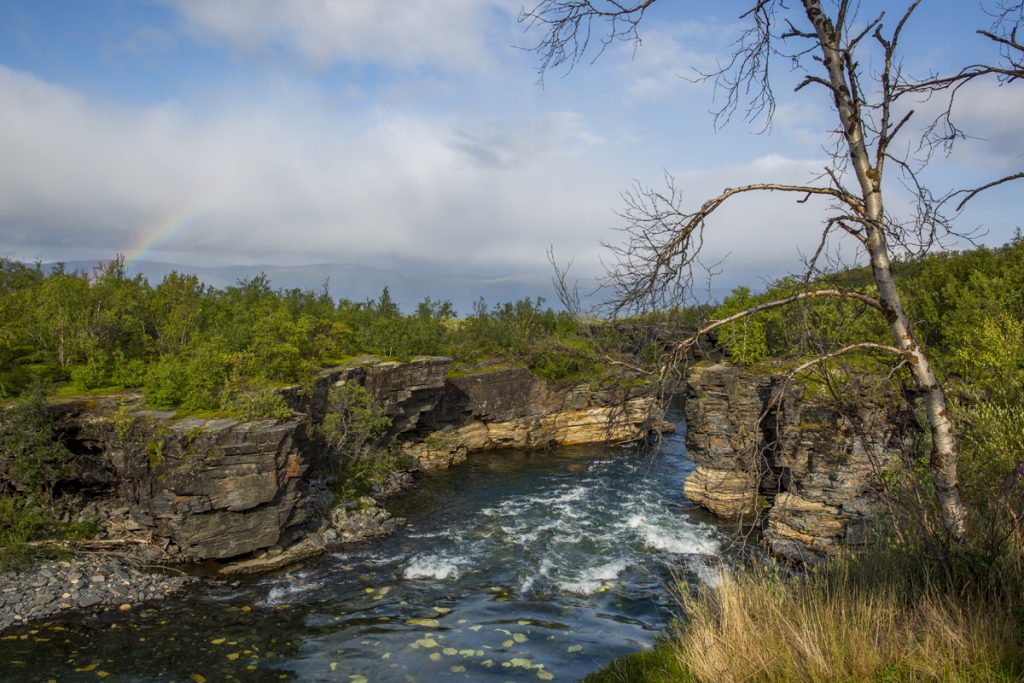 En liten regnbågen visar upp sina färger i den dramatiska naturen vid Abisko kanjon