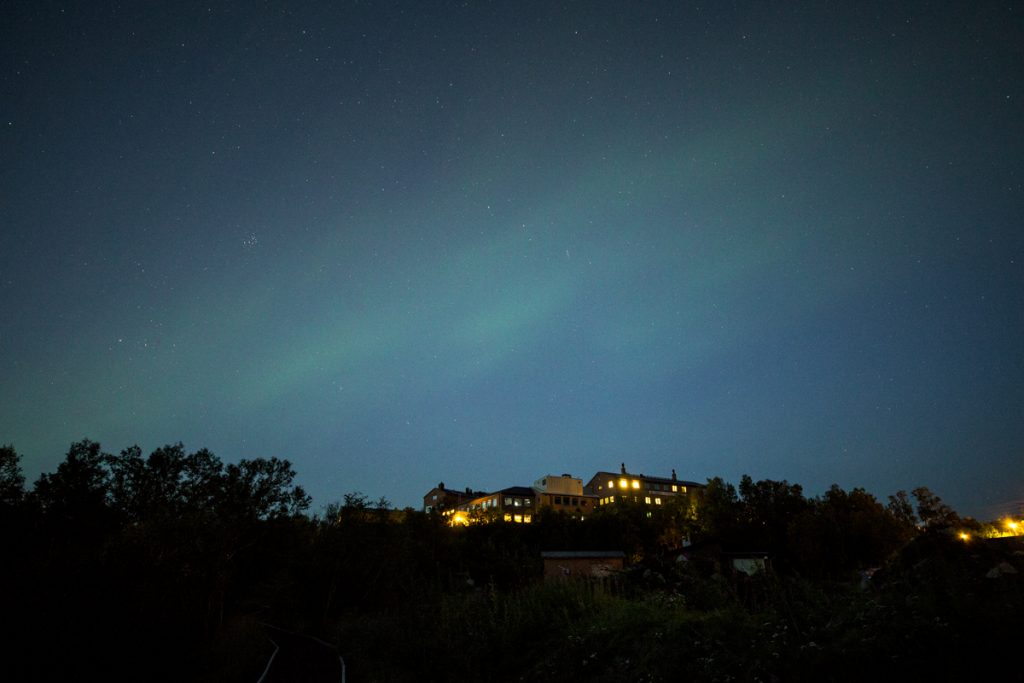 Ett försiktigt Norrsken dansar på himlen en klar natt över turisthotellet i Abisko